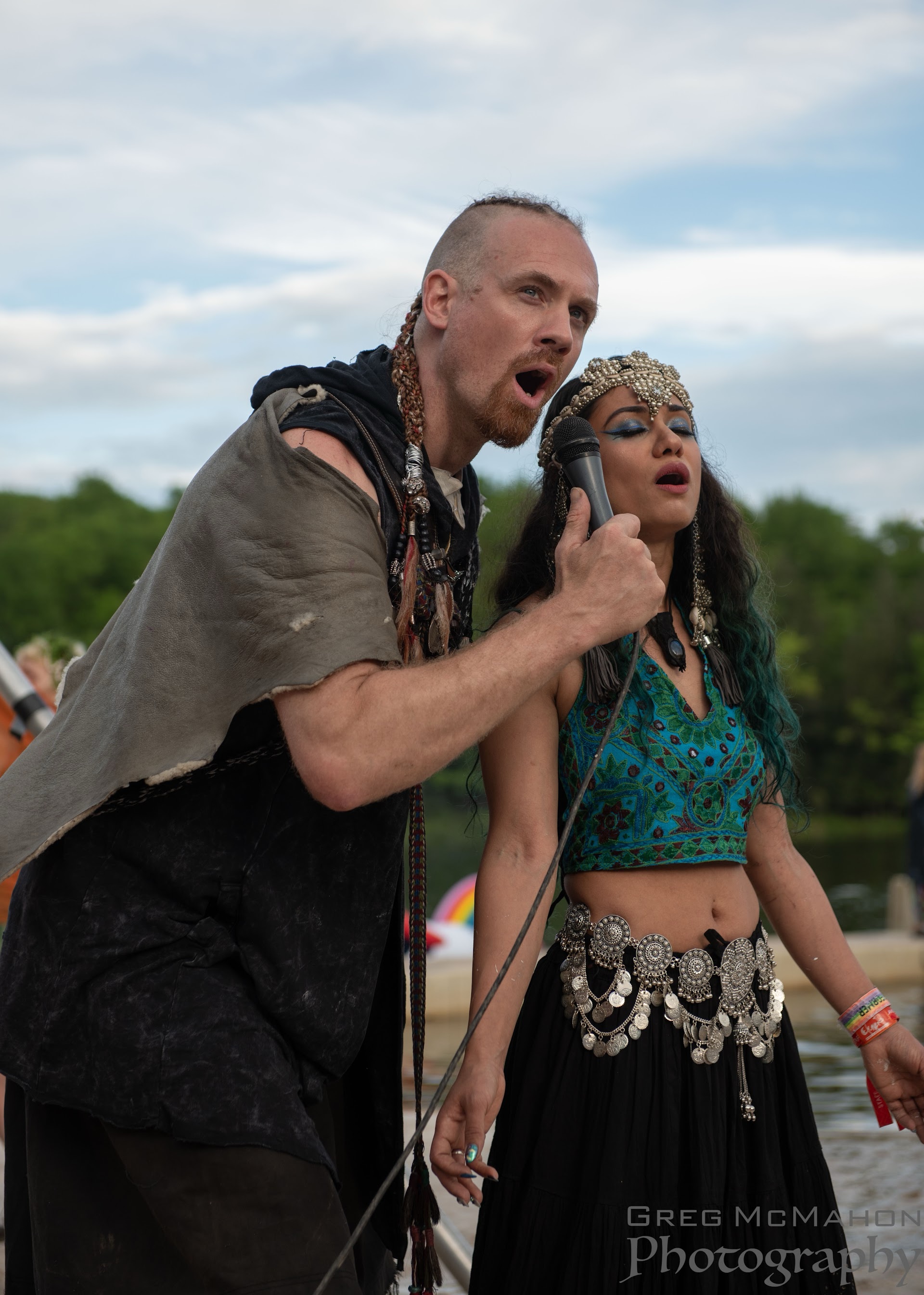 John and Radhika sharing a microphone during an outdoor performance; photograph by Greg McMahon