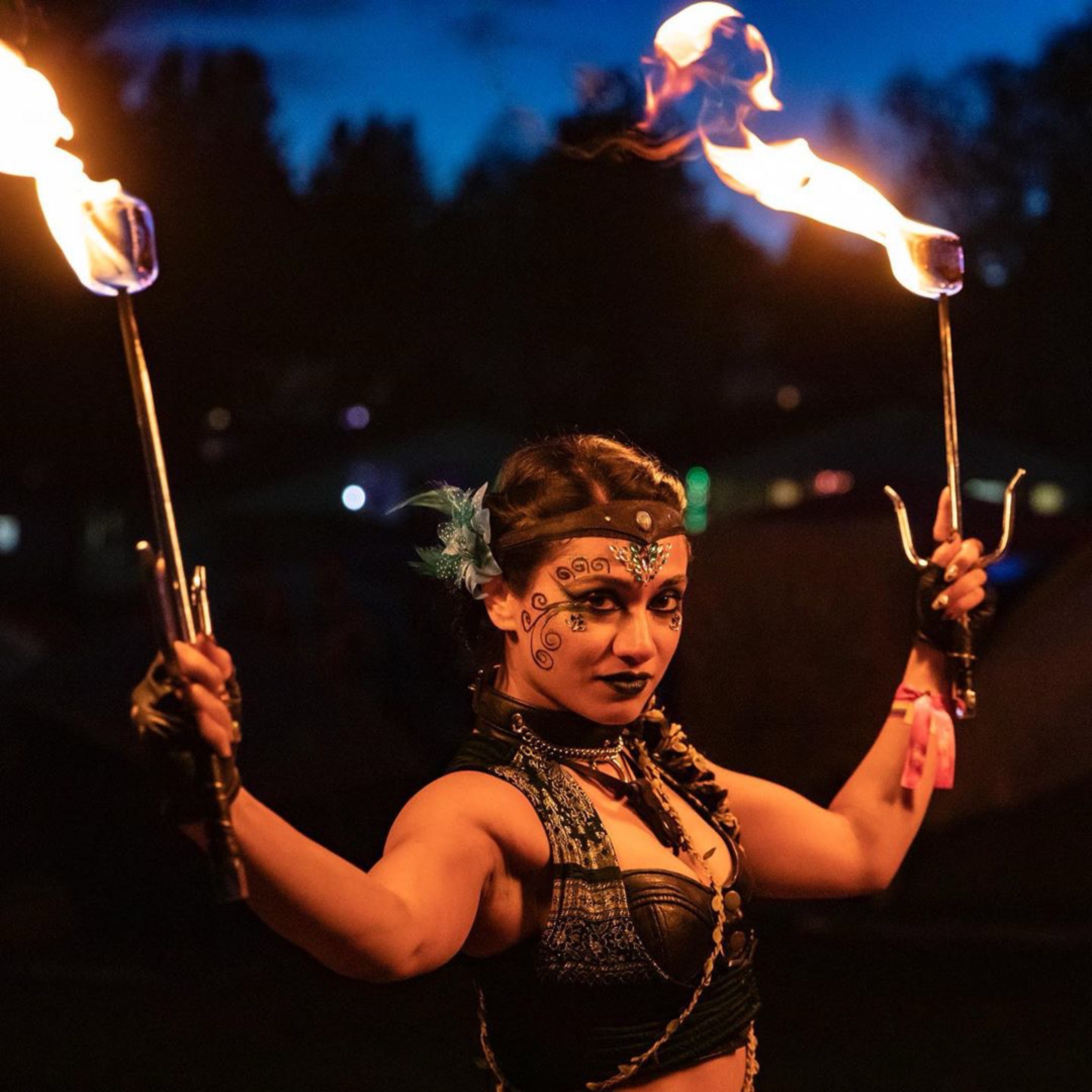 Radhika holding two flaming torches against the evening sky